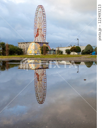 Reflection of a ferris wheel in a puddle. Resort town after the rain. Batumi ferris wheel. Amusement park. 122493213