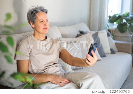 Mature beautiful middle-aged woman with gray hair and poor eyesight sits on the couch 122493766