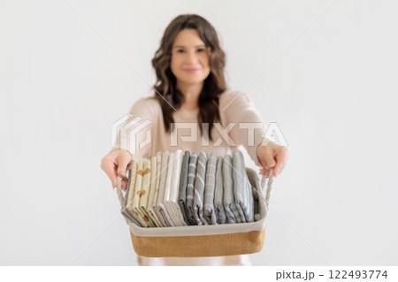 Beautiful European woman in beige suit holds wicker stylish basket with neatly folded pillowcases Beautiful European woman in beige suit holds wicker stylish basket with neatly folded pillowcases 122493774