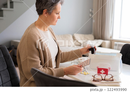 Container with pharmacy cure. Beautiful aged woman with gray hair checking medicines  122493990