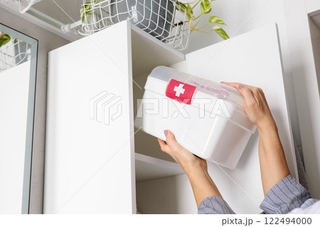 Female hands putting first aid kit with vitamins, drugs, antibiotics and cure at bathroom cupboard. 122494000