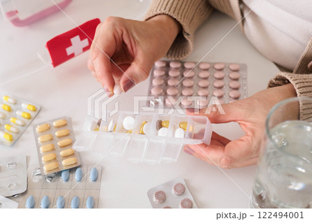 Closeup female hand neatly placing medicament at domestic first aid kit top view. 122494001
