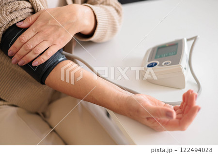 A woman in a blue shirt measures her blood pressure with a tonometer on a white table A woman in a blue shirt measures her blood pressure with a tonometer on a white table 122494028