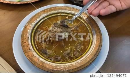 A Hand Serving a Spoonful of Traditional Turkish Kelle Paca Soup from Ornate Bowl 122494071