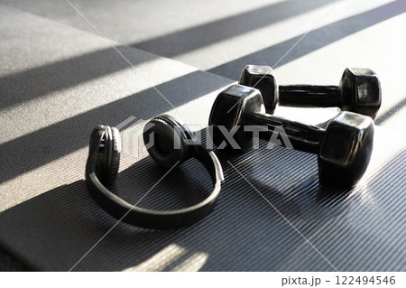 Concept of sports. Black headphones and dumbbells lie in the gym on a black yoga mat.  122494546