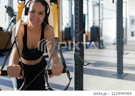 Young beautiful Asian woman doing fitness exercises with TRX exercise bands in gym. Young beautiful Asian woman doing fitness exercises with TRX exercise bands in gym. 122494564