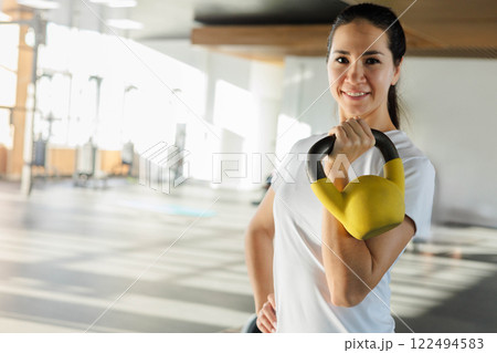 Portrait of muscular female athlete smiling posing with kettlebell training at modern gym closeup. 122494583