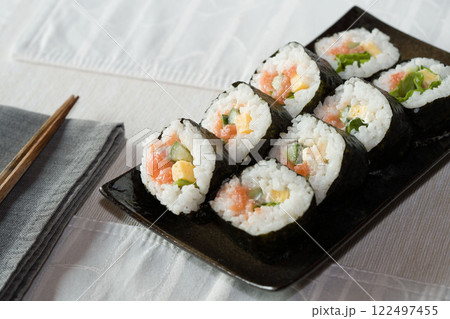 Homemade salmon salad sushi on black plate with white placemat on table. Japanese healthy food. Selective focus. Homemade salmon salad sushi on black plate with white placemat on table. Japanese healthy food. Selective focus. 122497455