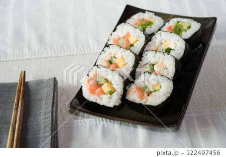 Homemade salmon salad sushi on black plate with white placemat on table. Japanese healthy food. Selective focus. Homemade salmon salad sushi on black plate with white placemat on table. Japanese healthy food. Selective focus. 122497456