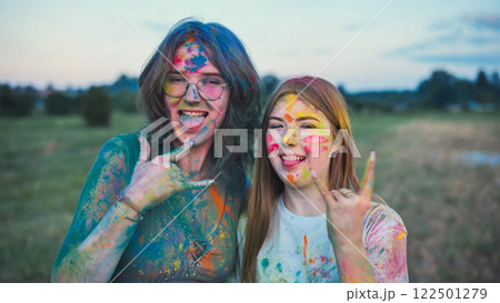 Two young women, covered in colorful powder paint, are enjoying the holi festival, sticking their tongues out and making the rock and roll hand sign Two young women, covered in colorful powder paint, are enjoying the holi festival, sticking their tongues out and making the rock and roll hand sign 122501279