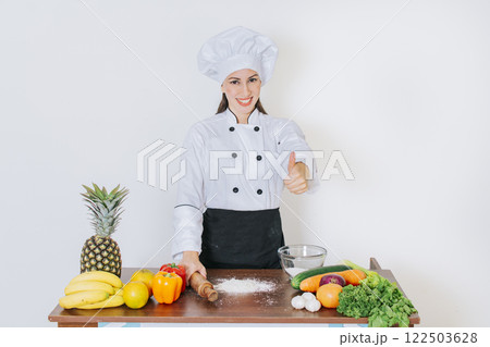 Chef woman holding bread rolling pin with thumb up, Smiling chef woman holding rolling pin on vegetable table, Concept of chef woman holding bread rolling pin Chef woman holding bread rolling pin with thumb up, Smiling chef woman holding rolling pin on vegetable table, Concept of chef woman holding bread rolling pin 122503628
