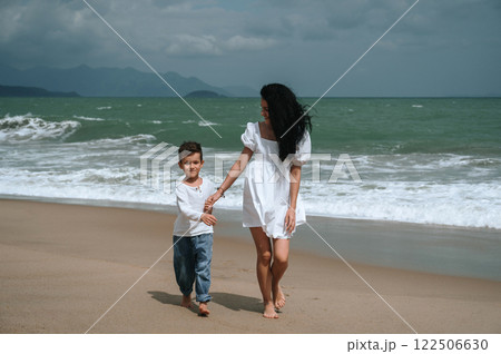 Happy mom and son walking along beach by the sea on summer vacation 122506630