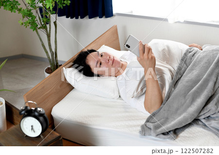 ベッドで寝ながら笑顔でスマホを使う男性 122507282