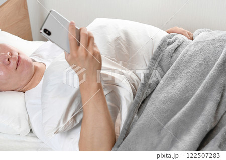 ベッドで寝ながら笑顔でスマホを使う男性 122507283