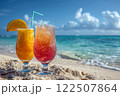 two different cocktails stand in the sand on the edge of the water on a perfect beach in the sand against the backdrop of the blue ocean 122507864