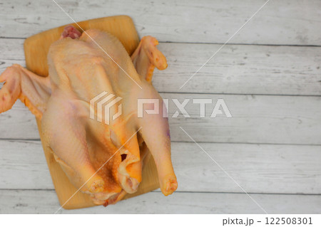 Close-up top view of a butchered raw chicken lying on a wooden cutting board against a white wood background with space for text. The concept of cooking, diet menu, ingredients. High quality photo 122508301