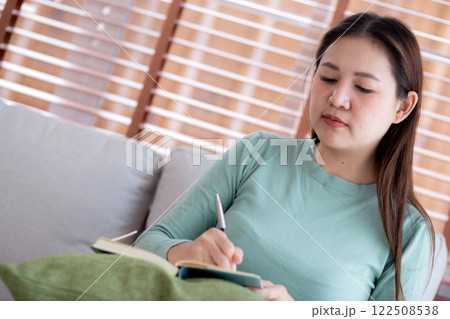 Happy young asian woman writing on book sitting on sofa with relax in living room at home. Happy young asian woman writing on book sitting on sofa with relax in living room at home. 122508538