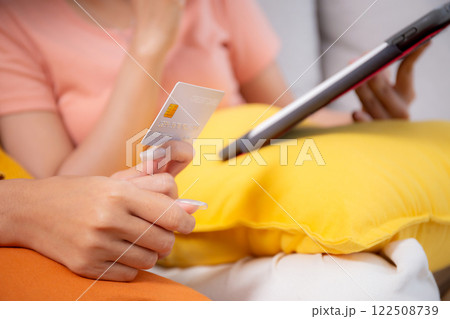 Closeup hand two young woman sitting on sofa using tablet computer shopping online with credit card. Closeup hand two young woman sitting on sofa using tablet computer shopping online with credit card. 122508739