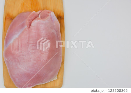 On a wooden cutting board lies a close-up piece of turkey meat on a white background with space for text. The concept of a diet menu, cooking. High quality photo On a wooden cutting board lies a close-up piece of turkey meat on a white background with space for text. The concept of a diet menu, cooking. High quality photo 122508863