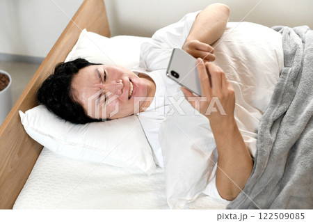 ベッドの上でスマホを持ちながら困る男性 ベッドの上でスマホを持ちながら困る男性 122509085
