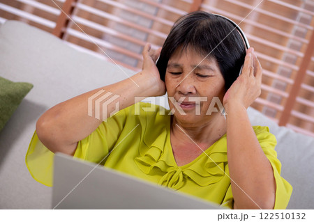 Happy senior asian woman wearing headphones listening music while sitting on sofa with fun and enjoy Happy senior asian woman wearing headphones listening music while sitting on sofa with fun and enjoy 122510132