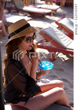 Elegant woman sipping blue cocktail at tropical beach  122510167