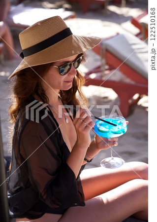 Woman in sun hat relaxing with blue cocktail on beach  122510168
