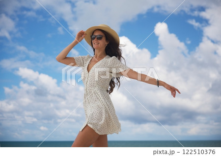 Joyful woman in sun hat dancing by the ocean  122510376