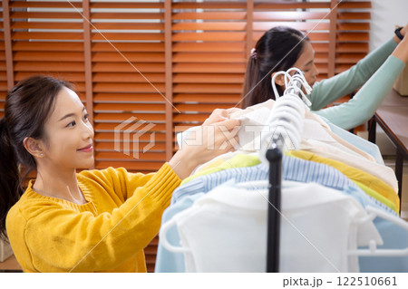 Two young asian woman arranging clothes in store for preparation delivery, seller choice clothes. Two young asian woman arranging clothes in store for preparation delivery, seller choice clothes. 122510661