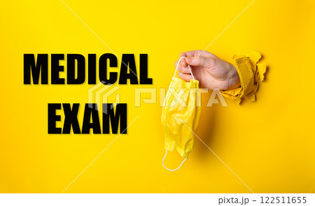 A person holding a yellow medical mask with the words medical exam below A person holding a yellow medical mask with the words medical exam below 122511655