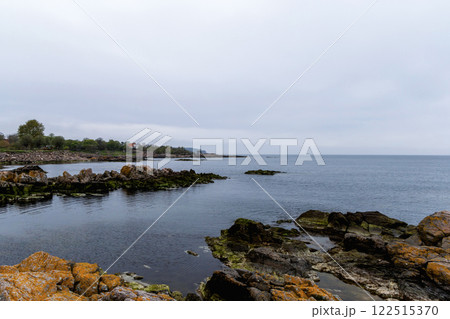 Coast line of sea. Stones covered with yellow and green moss and cloudy sky. 122515370