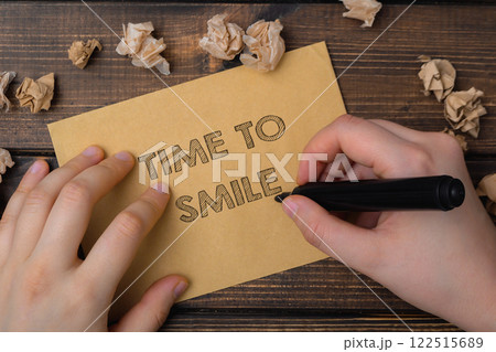 Hand is writing on a piece of paper that says Time to smile. Hand is writing on a piece of paper that says Time to smile. 122515689
