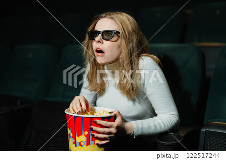 Excited viewer enjoying a movie in a dark theater with popcorn 122517244