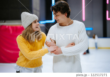 Couple enjoys skating and laughter at indoor ice rink during winter afternoon Couple enjoys skating and laughter at indoor ice rink during winter afternoon 122517271