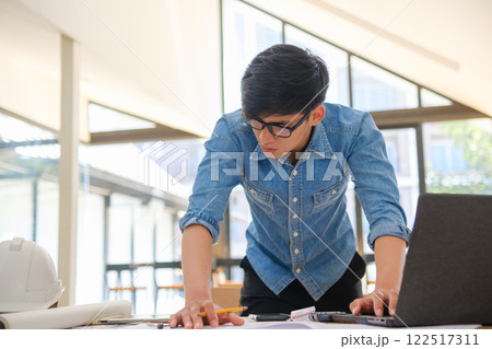 Young architect sketching house plans on a work desk in a modern office Young architect sketching house plans on a work desk in a modern office 122517311
