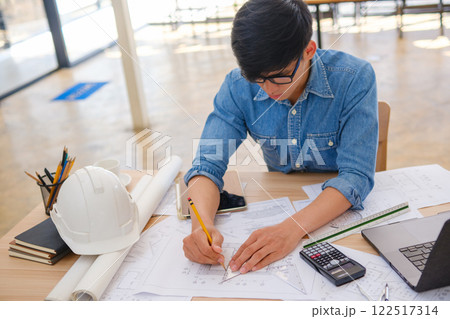 Young architect sketching house plans on a work desk in a modern office Young architect sketching house plans on a work desk in a modern office 122517314