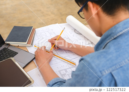 Young architect sketching house plans on a work desk in a modern office Young architect sketching house plans on a work desk in a modern office 122517322