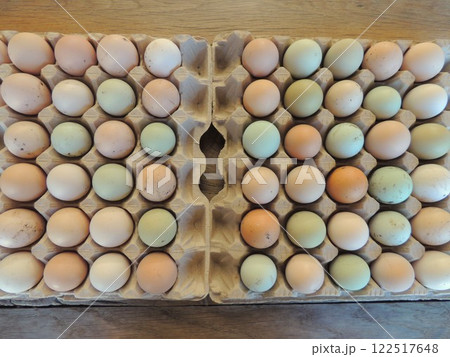 colored eggs of domestic hens of different breeds lying in cardboard cells on a wooden table, seen from above, selected chicken eggs for incubation with dirty multi-colored shells 122517648
