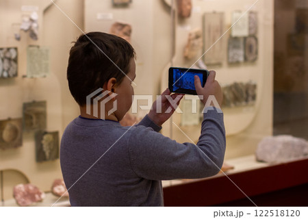 The young student explores the museum exhibition and takes pictures of artifacts with a smartphone, enjoying cultural and educational experience. A teenager at the museum on excursions. 122518120