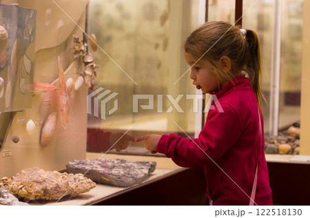 A little girl indicating interesting shells and fossils for a glass demonstration in the Museum of Natural History, enjoying educational and exciting experience. The child is in the museum. 122518130