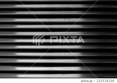 The parallel metal bars of the ventilation grille create a repeating pattern, enhanced by the play of light and shadow, adding depth and texture to the metal surface. Metal grille background. The parallel metal bars of the ventilation grille create a repeating pattern, enhanced by the play of light and shadow, adding depth and texture to the metal surface. Metal grille background. 122518139