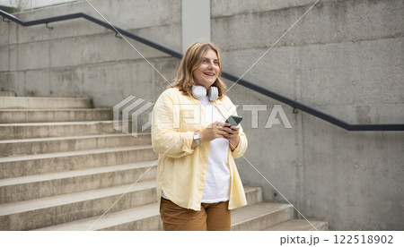 Happy young woman with mobile standing on steps in city. Holidays, technology and tourism concept. Female tourist searching direction on smart phone while traveling abroad in summer Happy young woman with mobile standing on steps in city. Holidays, technology and tourism concept. Female tourist searching direction on smart phone while traveling abroad in summer 122518902