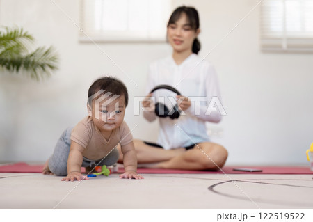Multitasking mother supervising her crawling baby while preparing for meditation with headphones at home Multitasking mother supervising her crawling baby while preparing for meditation with headphones at home 122519522