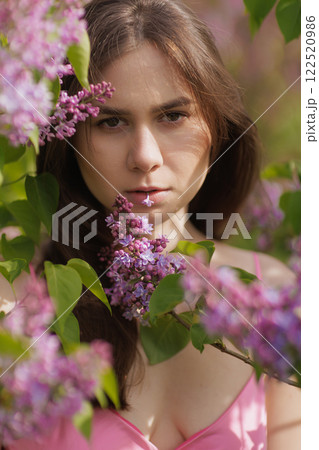 A woman in a pink dress stands among blooming lilac bushes, enjoying the spring atmosphere. relaxation and pleasure, 122520986