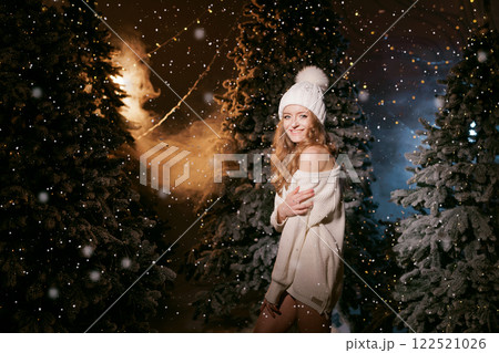 A woman in winter clothing sits on a snowy ground surrounded by decorated Christmas trees, with snowflakes falling gently around her. 122521026