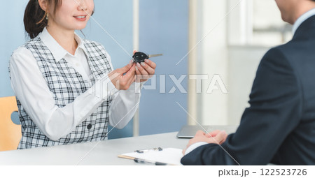 受付で車の鍵の受け渡しをする女性スタッフと顧客の男性 122523726