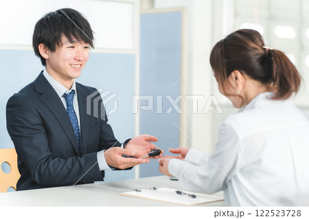 受付で車の鍵の受け渡しをする男性スタッフと顧客の女性 122523728