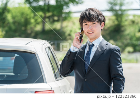 車の隣でスマホで通話するスーツ姿のビジネスマン（自動車保険・予約・買取・査定・下取り） 122523860