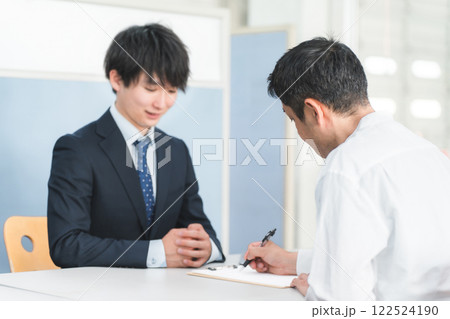 受付・窓口で男性客を接客する若いアジア人ビジネスマンとサインをする顧客 受付・窓口で男性客を接客する若いアジア人ビジネスマンとサインをする顧客 122524190