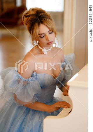 Elegant woman in a light blue ball gown in a luxurious classic interior plays a white piano Elegant woman in a light blue ball gown in a luxurious classic interior plays a white piano 122524643